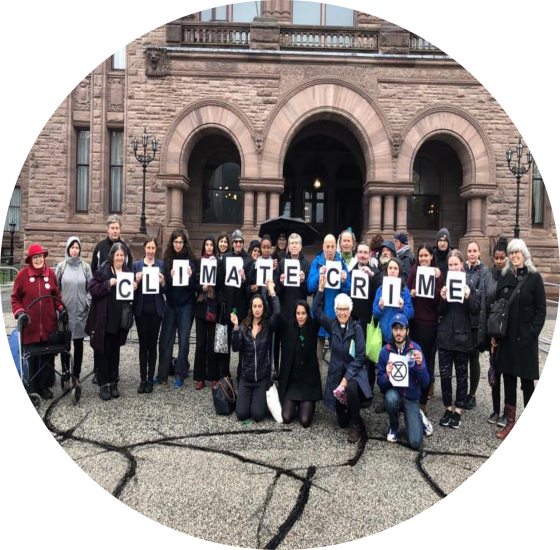 group of people outside Queen's Park with letters spelling Climate Crime